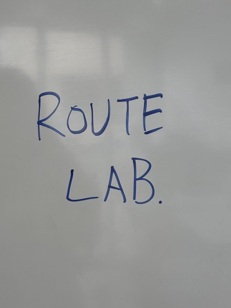 「ROUTE LAB.」と書かれたホワイトボードや黒板の文字、または授業中に使われたワークシート的なもの。スクール内の雰囲気が伝わるもの