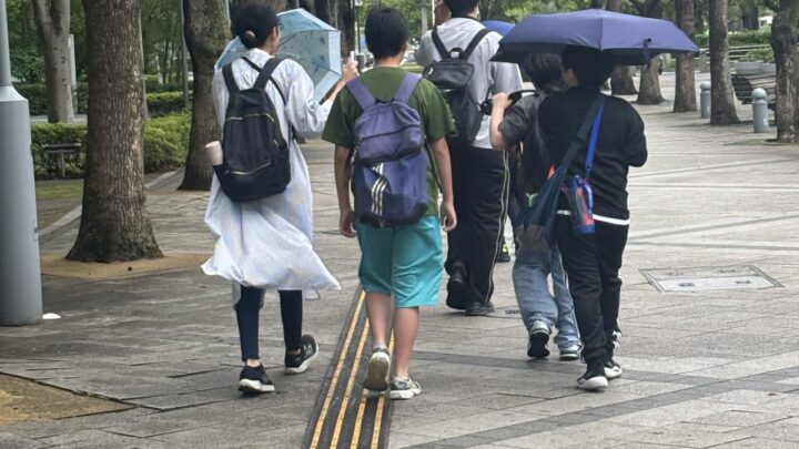 窓際の明るい席で、女の子がタブレットや教材を使って自分のペースで学習している様子。スタッフが少し離れたところで見守っている構図。
