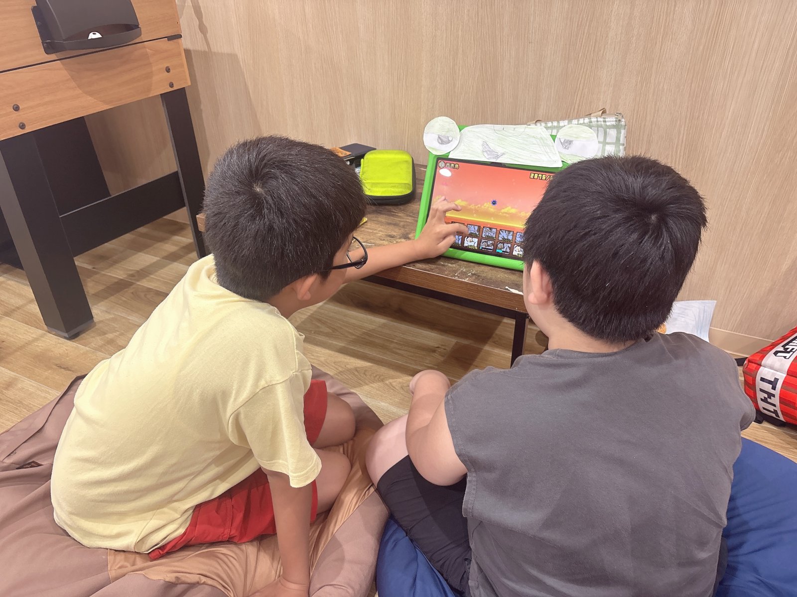 スタッフと子どもが穏やかに並んでPCやタブレットを見ている様子。温かみのある室内、自然光が入る明るい空間