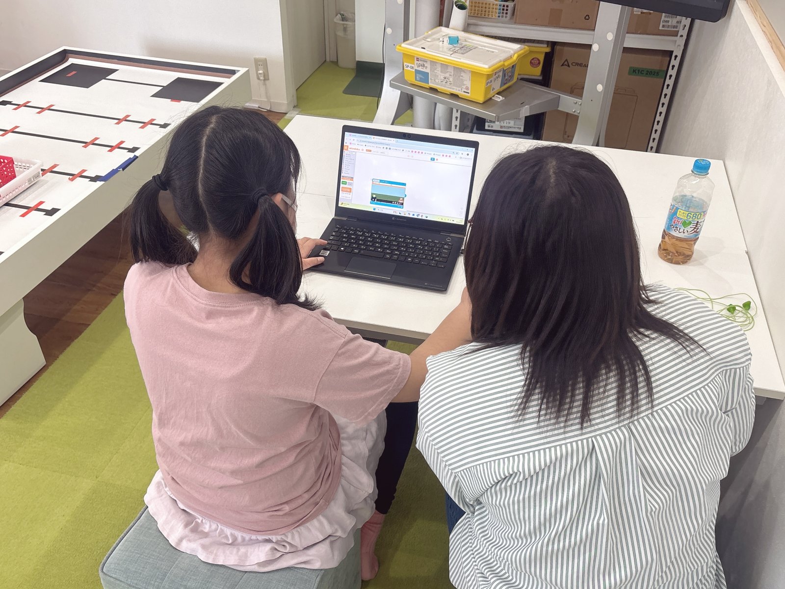 スタッフが子どもの隣に座り、ノートやタブレットを一緒に見ながら穏やかに話している場面。上から教えるのではなく、横に並んでいる雰囲気