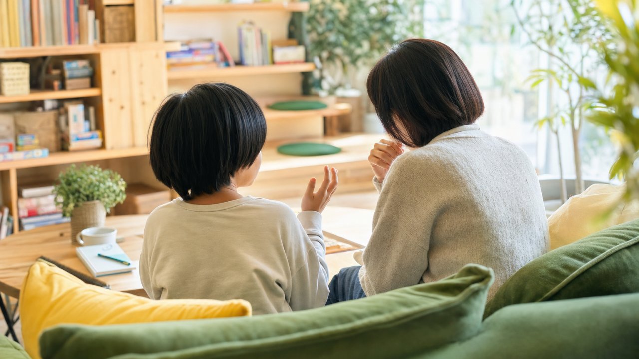 子どもと保護者が並んでソファに座り、穏やかに話をしている様子。温かみのある自然光。サムネイル用メイン画像