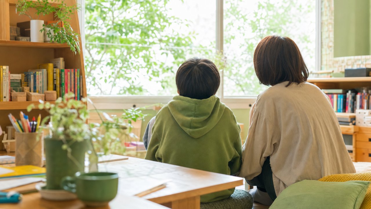 窓の外を穏やかに見つめる子どもと、そのそばで寄り添うように座っている保護者のイメージ写真（サムネイル用）