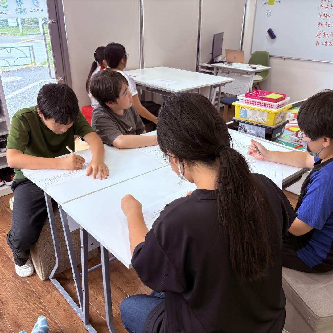 子どもたちがテーブルを囲んで、スタッフと一緒に話し合っているようす。付箋やホワイトボードが見える和やかな場面