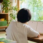 カレンダーの8月・9月のページが写っていて、子どもがじっとそれを見ているような後ろ姿のイメージ。重さや不安を静かに表現