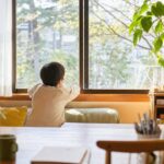 子どもが窓の外をぼんやり眺めている後ろ姿。静かで穏やかな雰囲気。「言葉にならない気持ち」を表現するイメージ