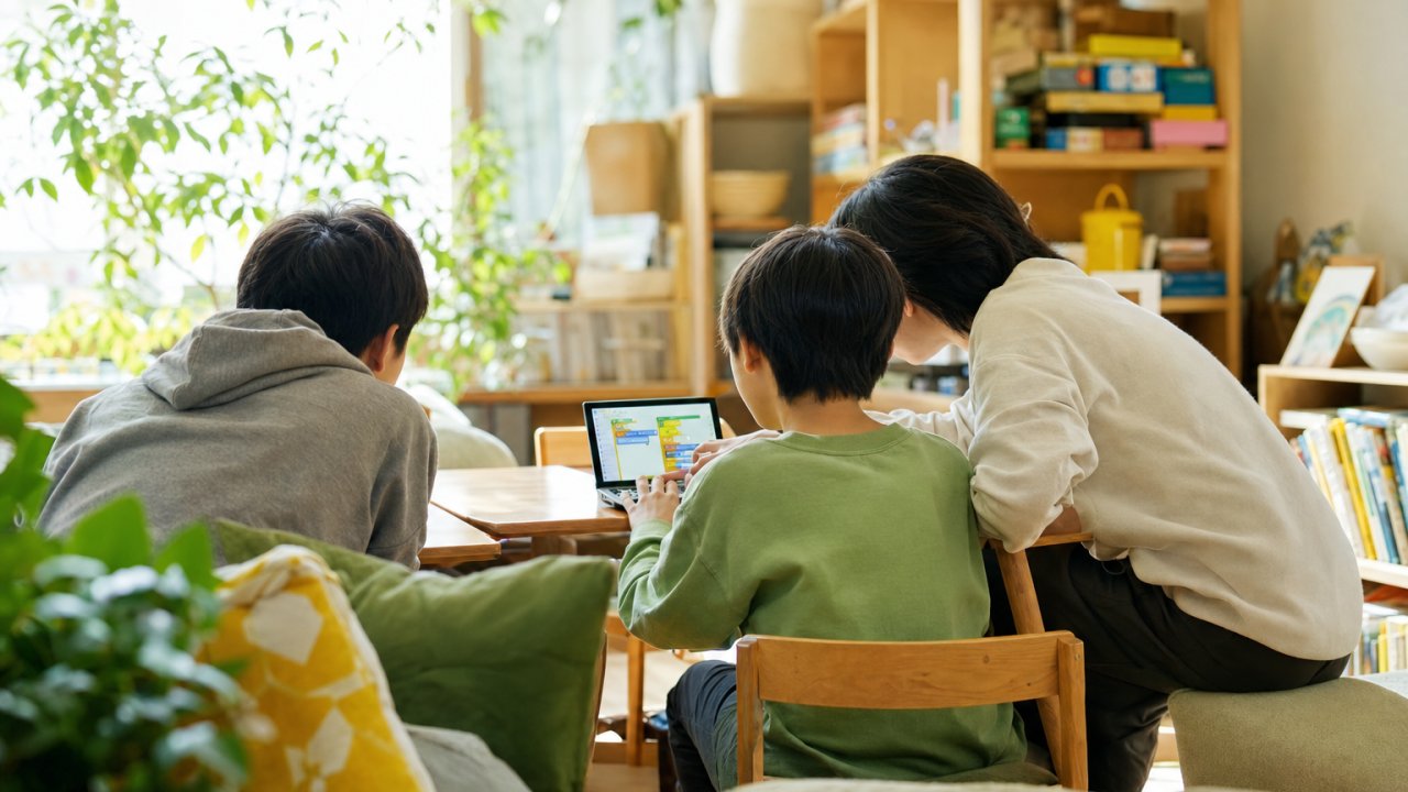 スタッフと子どもが一緒にボードゲームかプログラミングに取り組んでいる様子。楽しそうな雰囲気で、学校のことは関係なさそうな日常の一コマ