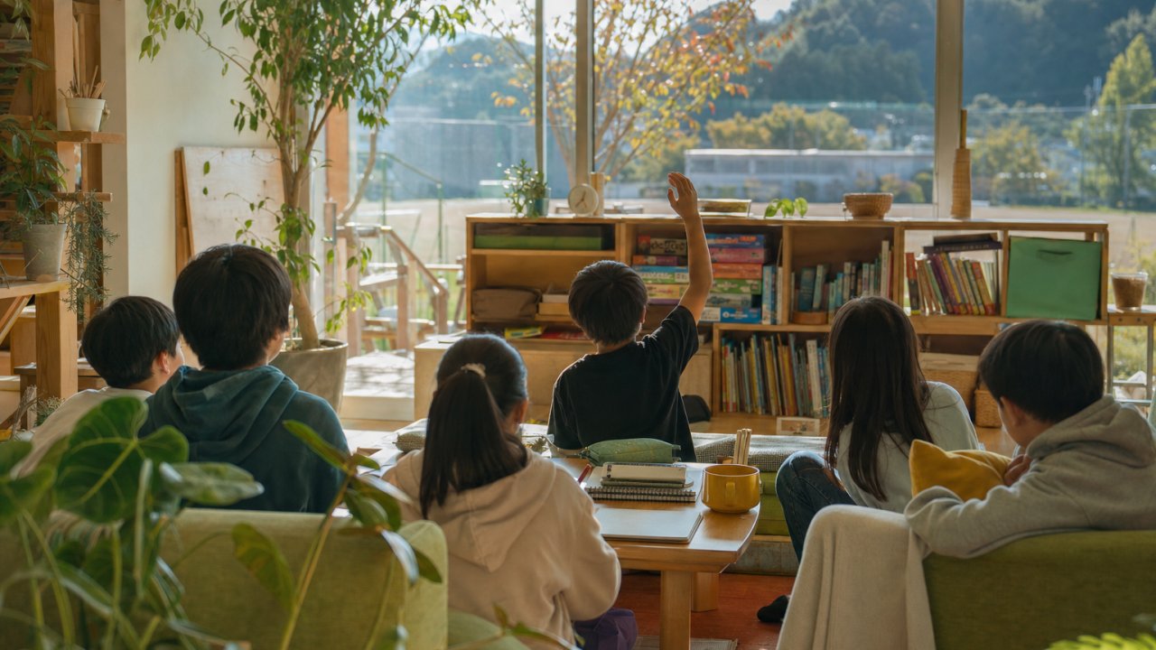 秋の空と学校のグラウンドを遠くから穏やかに眺めるような写真。子どもの後ろ姿や、葉が少し色づき始めた木などがあると季節感が出る。サムネイル用