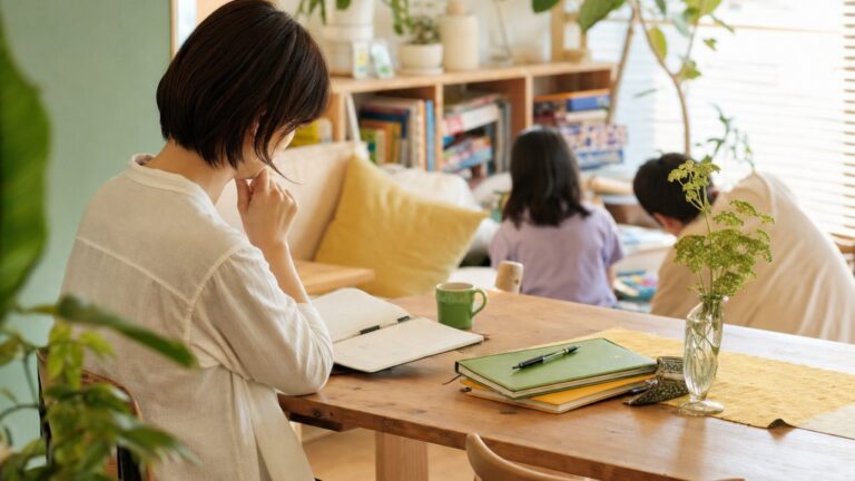 手帳やノートを前に考え込む保護者のイメージ。柔らかい光の中で、ひとりで向き合っている雰囲気