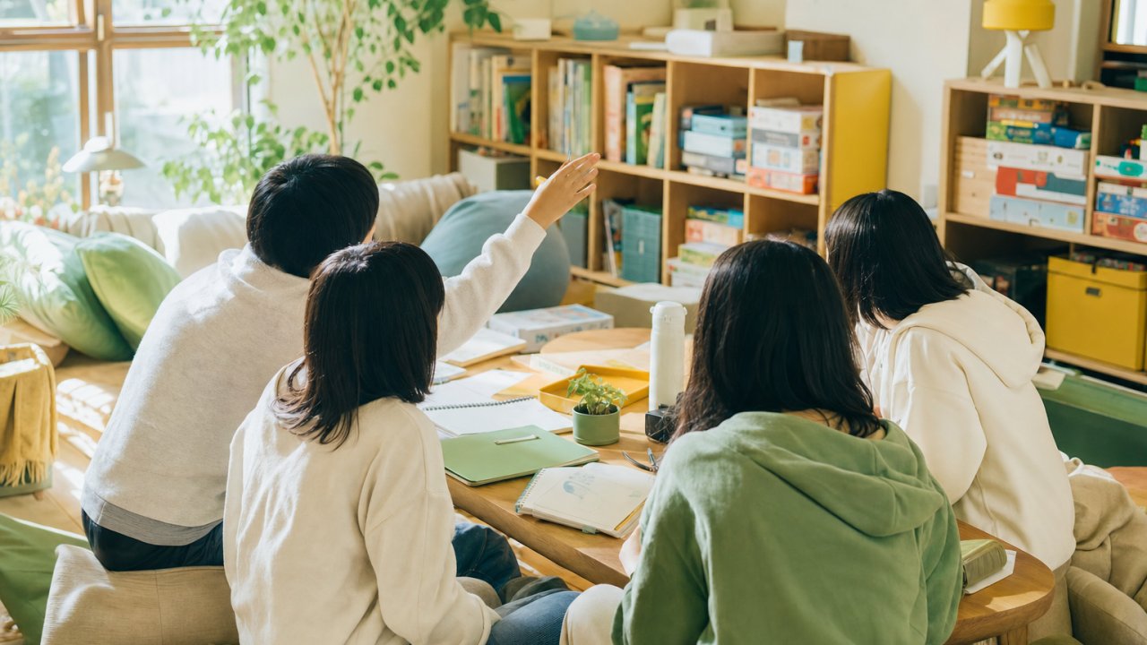 サムネイル｜スタッフが小学校・中学校の校門や受付付近で先生と笑顔で話しているイメージ。温かみのある自然光の写真